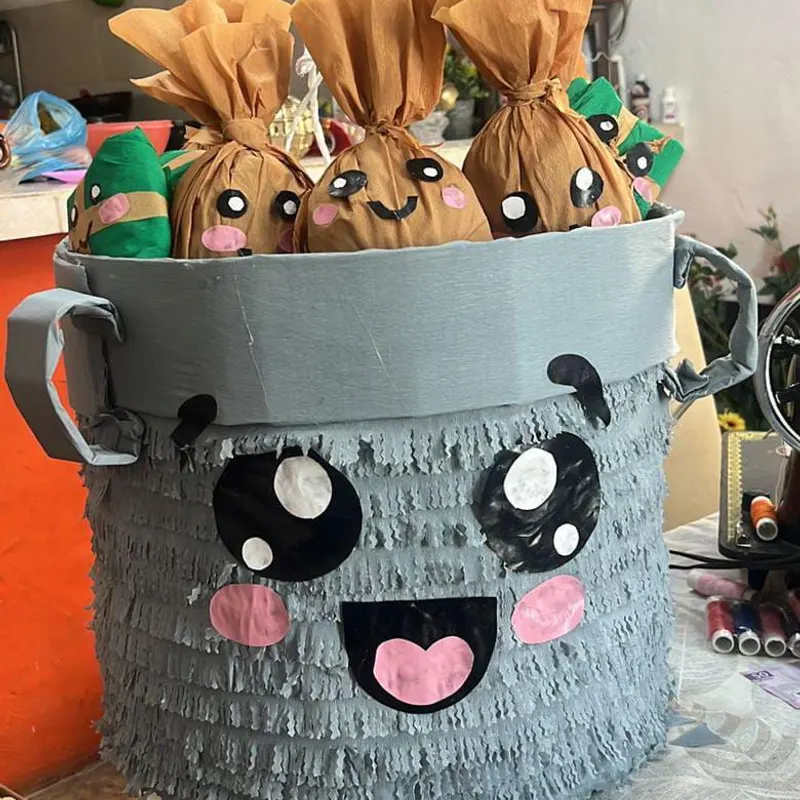 Piñata en forma de cubeta gris con carita, llena de bolsitas de dulces
