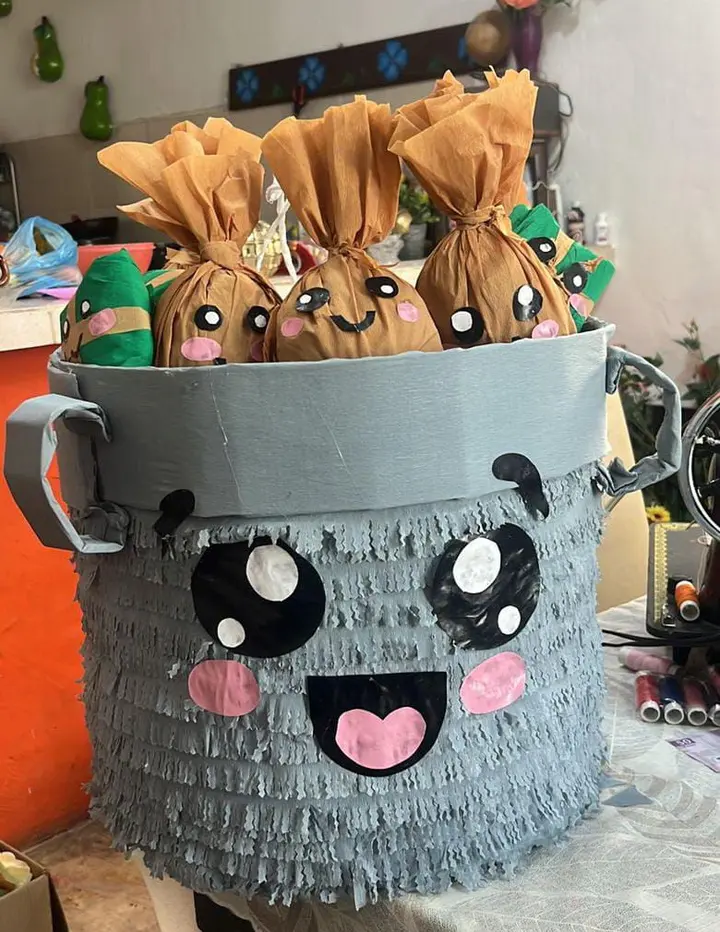 Piñata en forma de cubeta gris con carita, llena de bolsitas de dulces